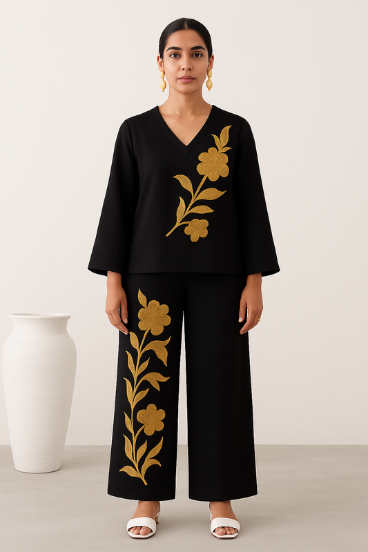 Woman wearing a black outfit with gold floral embroidery against a white background